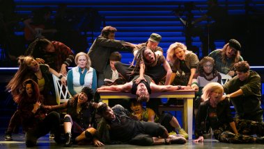 Elizabeth Stanley, seated near table at left, and Celia Rose Gooding, seated at right, with the ensemble of “Jagged Little Pill.” Photo by Sara Krulwich/The New York Times